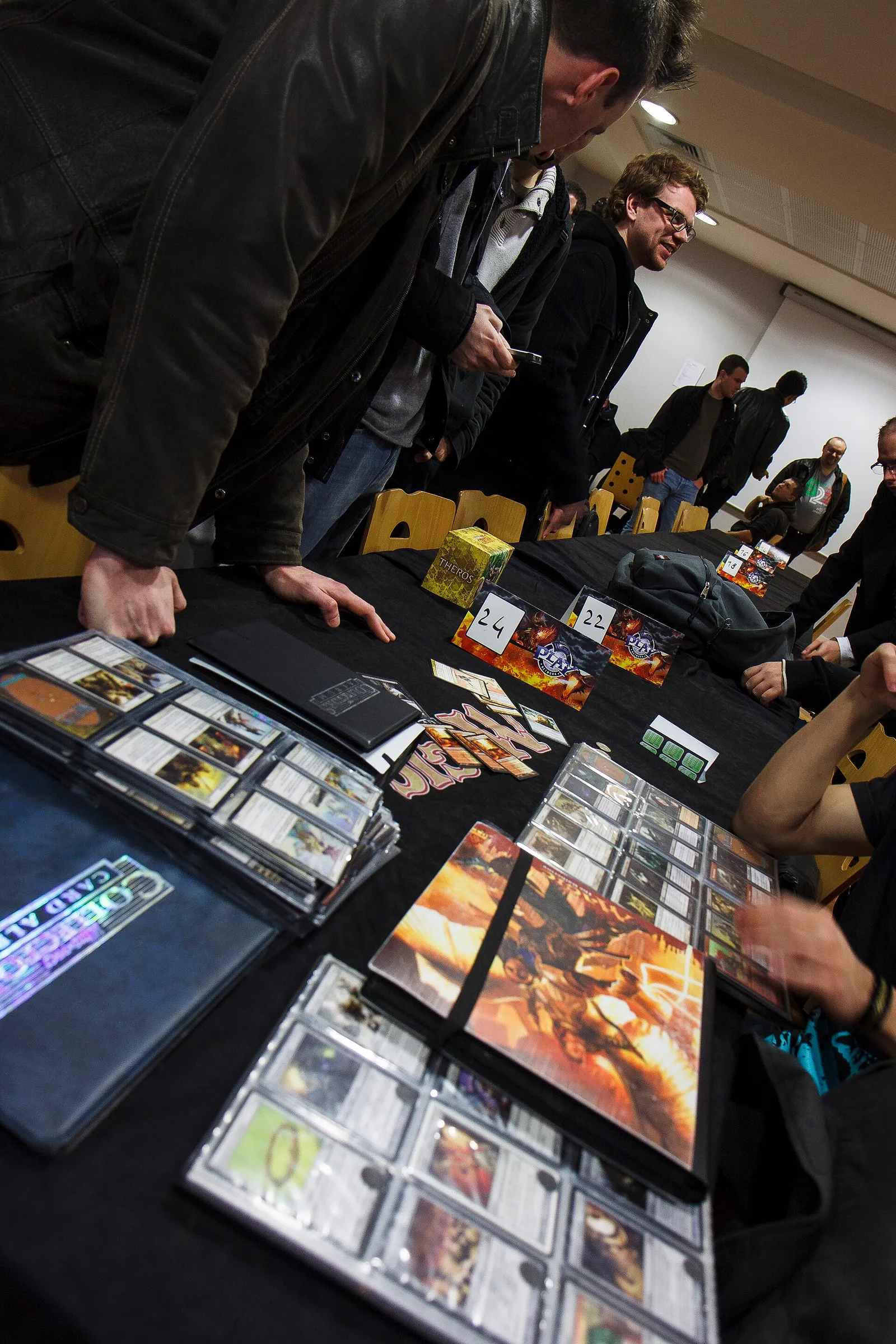 Gente inclinada sobre una mesa llena de archivadores abiertos con cartas de Magic: The Gathering.