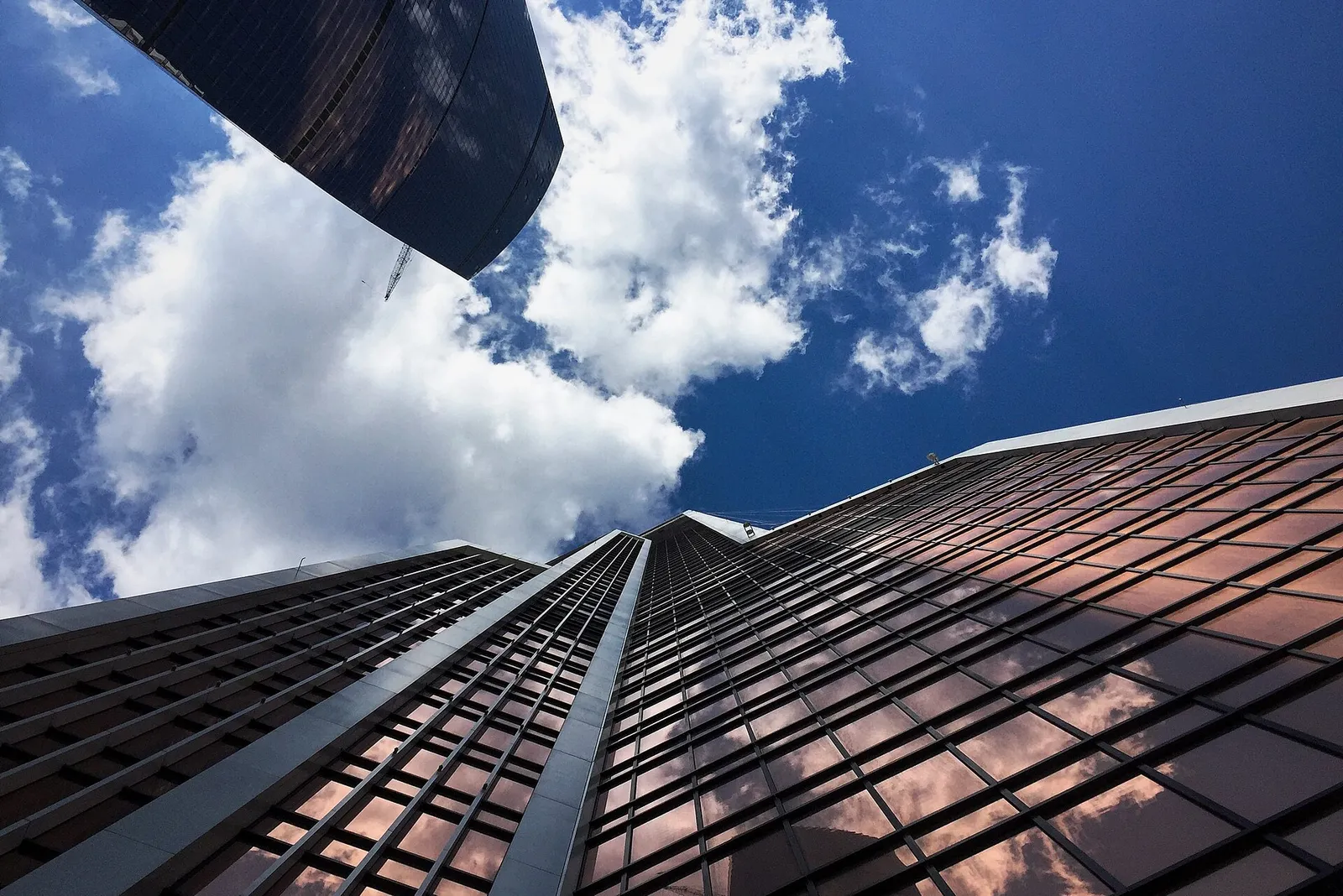 Os arranha-céus de vidro do Moscow City vistos de baixo, com nuvens refletidas nas janelas.