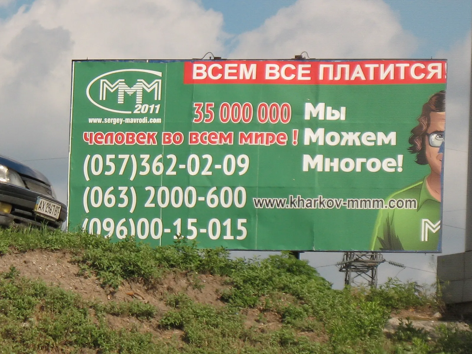 Зелёный рекламный щит у дороги: логотип «МММ 2011», надпись «Всем всё платится!», номера телефонов и мужчина в очках.