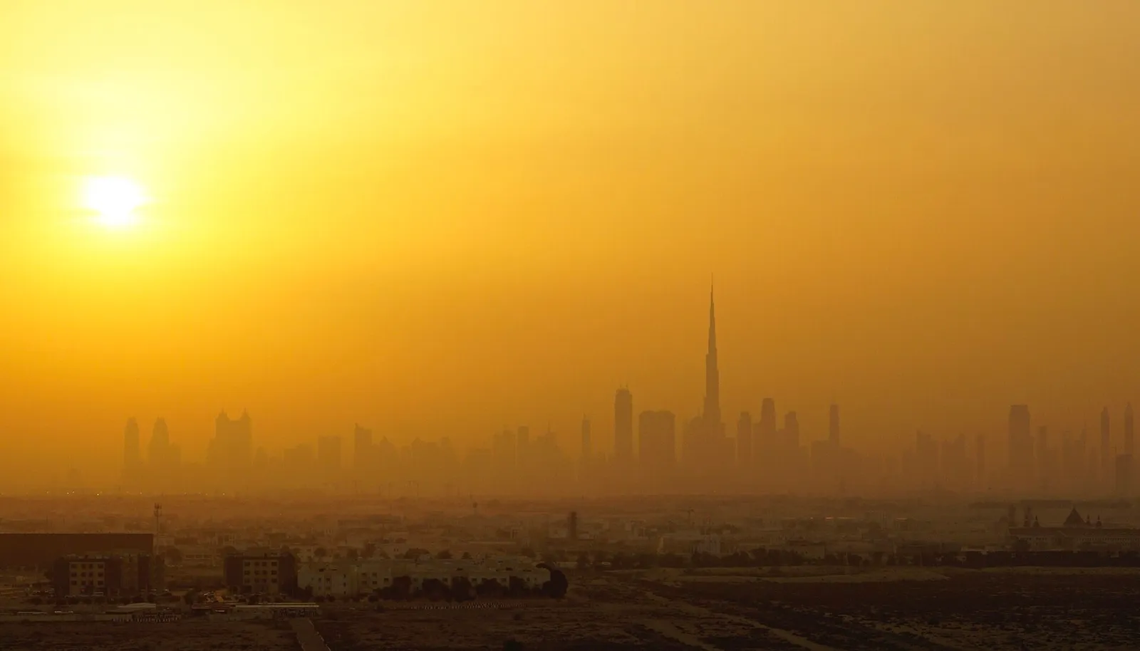 La silueta de Dubái con la aguja del Burj Khalifa en una bruma anaranjada, el sol bajo.