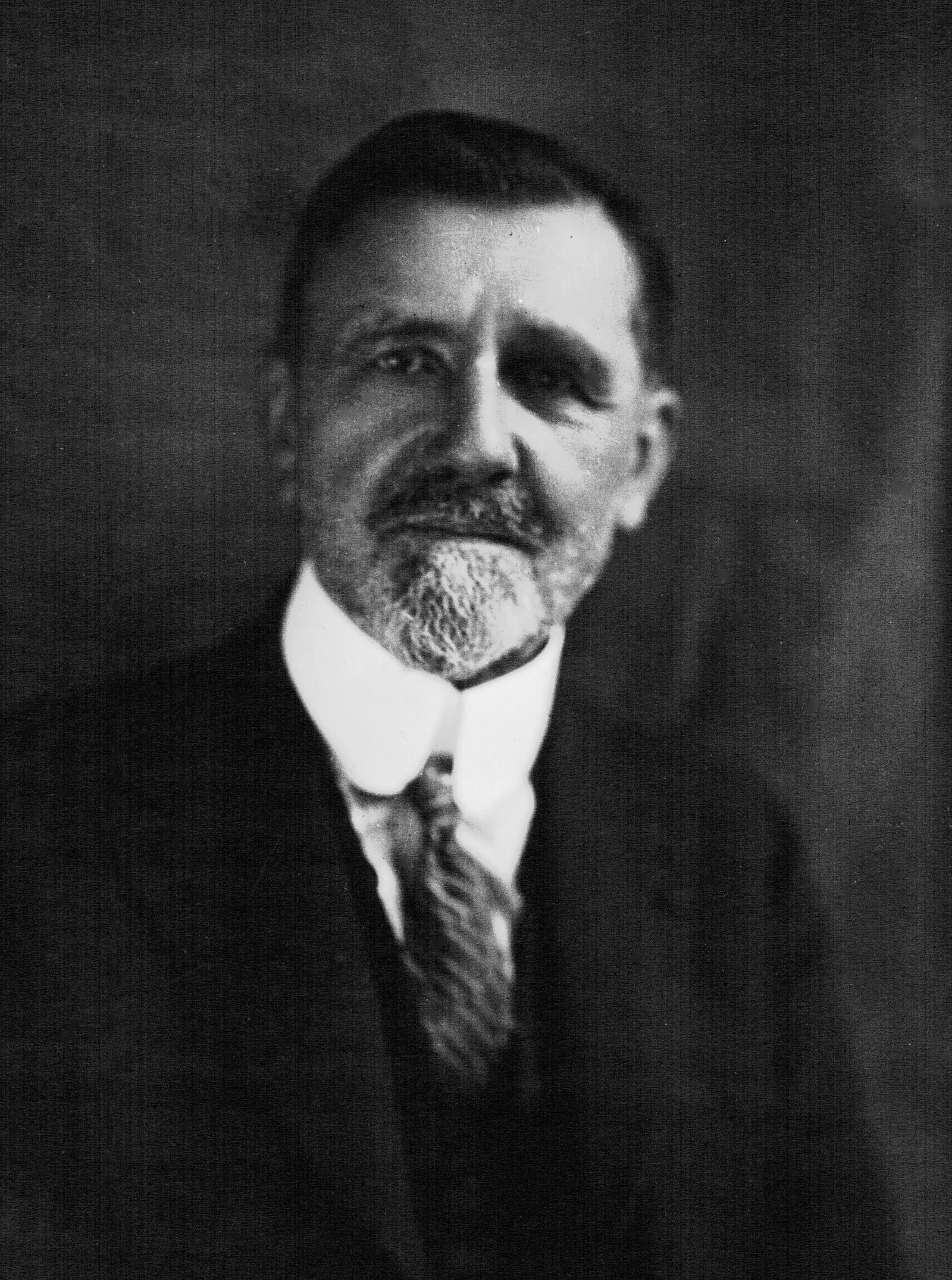 Retrato de um homem de idade com barba curta, de casaco e gravata.